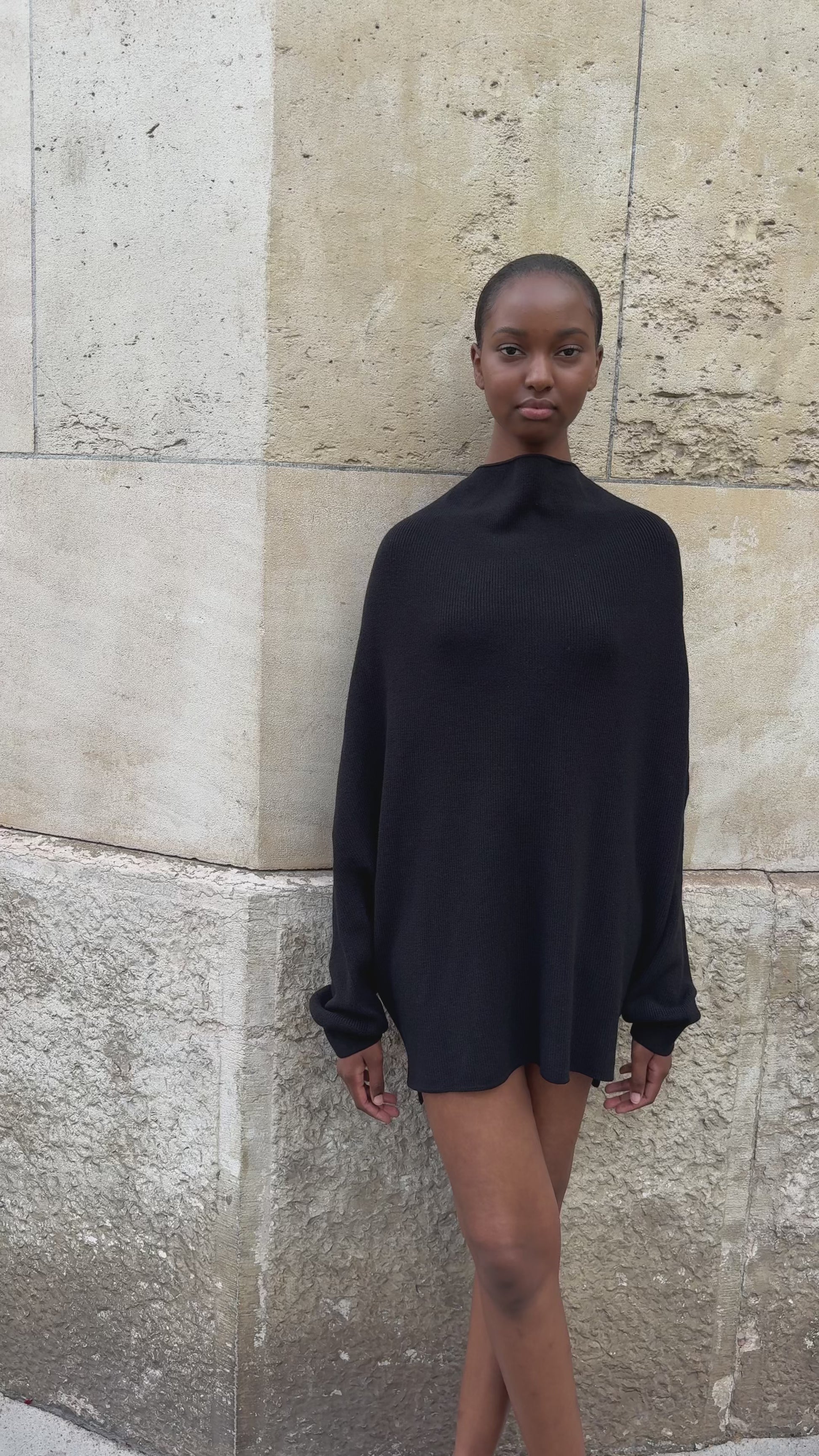 Female model against a stone wall wearing APAR Edition 002 - carre knit in black 